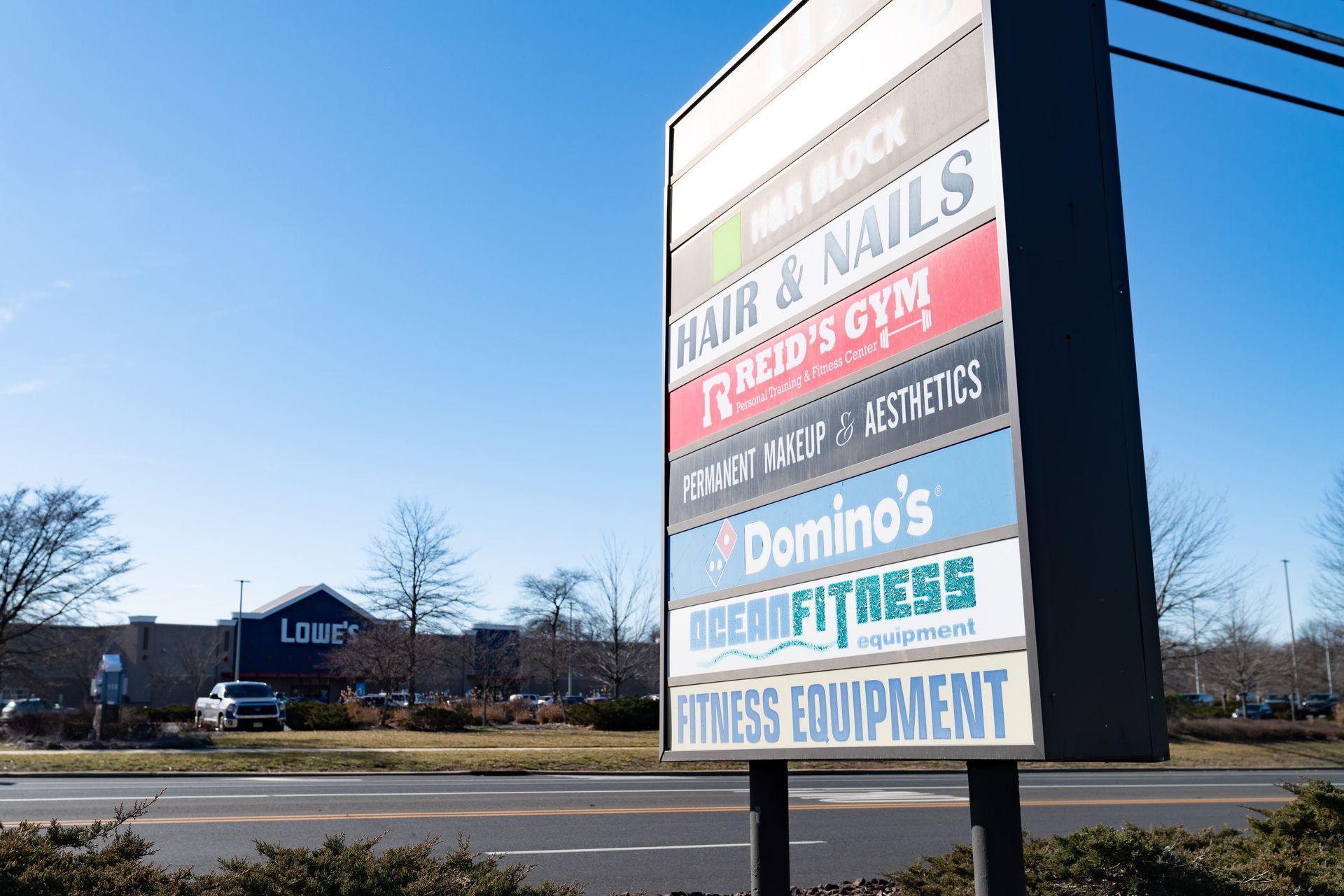 A tall commercial sign lists several businesses, including Domino's, above a road with a Lowe's store in the background.