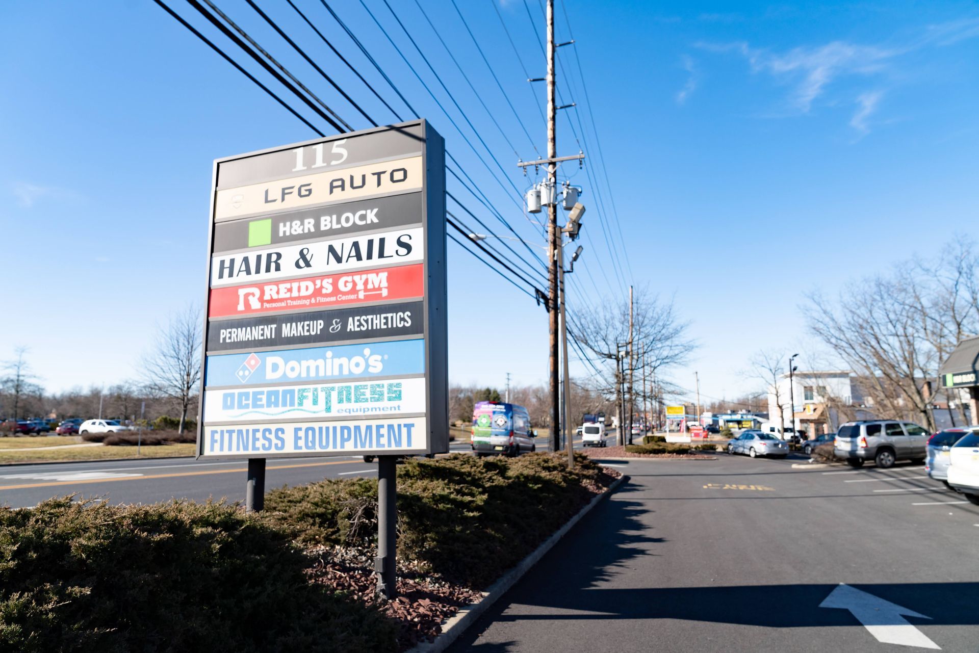 A directory sign for a shopping plaza stands in front of a parking lot under a clear blue sky.