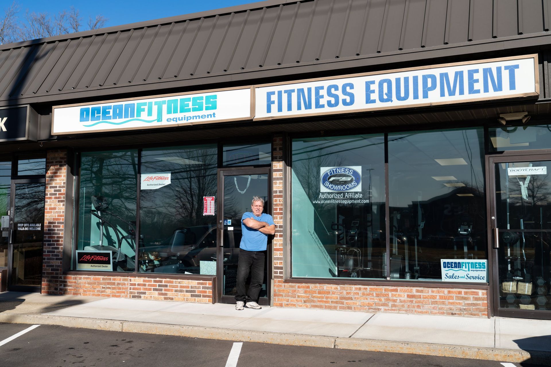 A person stands in the doorway of Ocean Fitness, a shop selling fitness equipment in a brick building.
