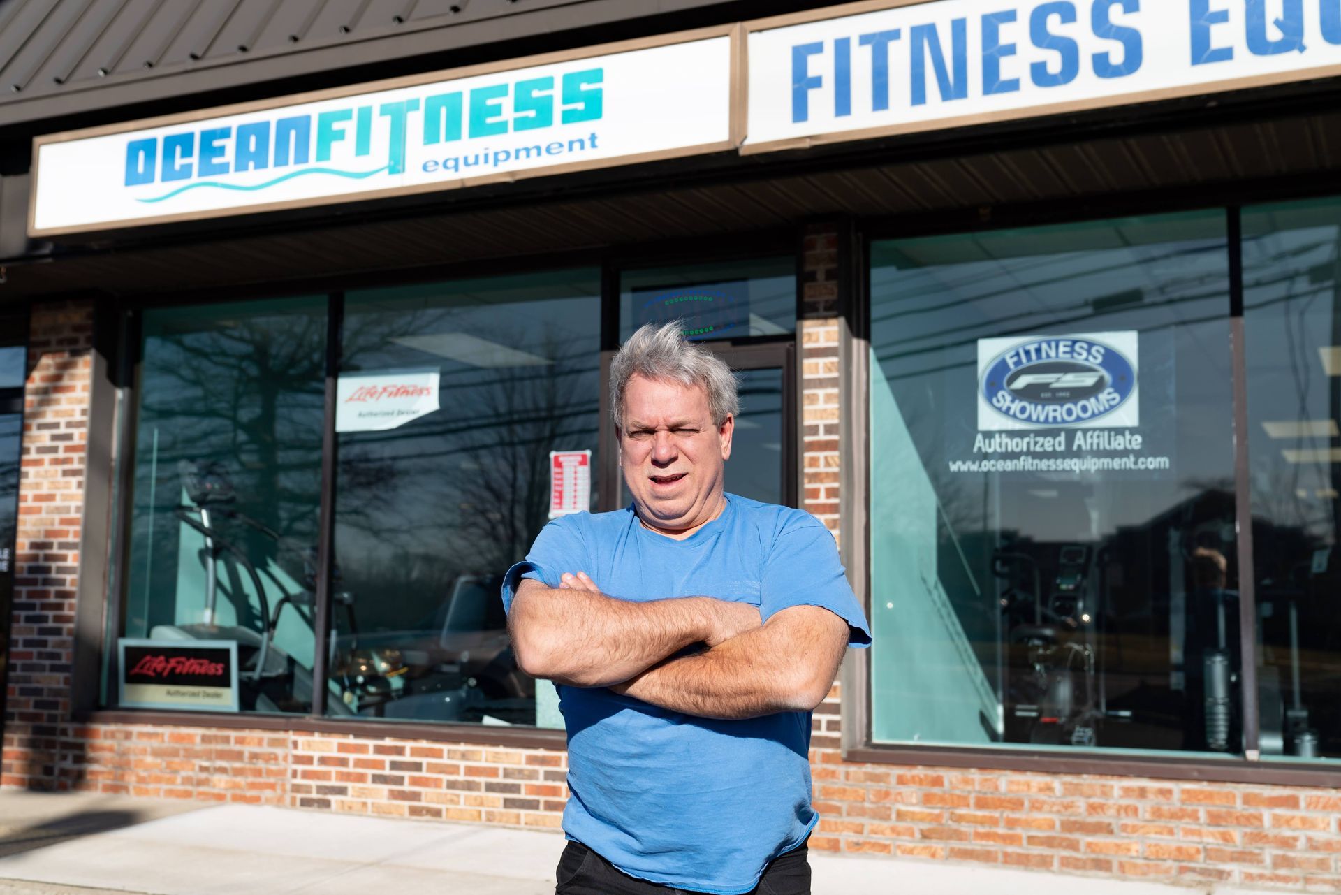 A person with crossed arms stands outside the Ocean Fitness Equipment store.