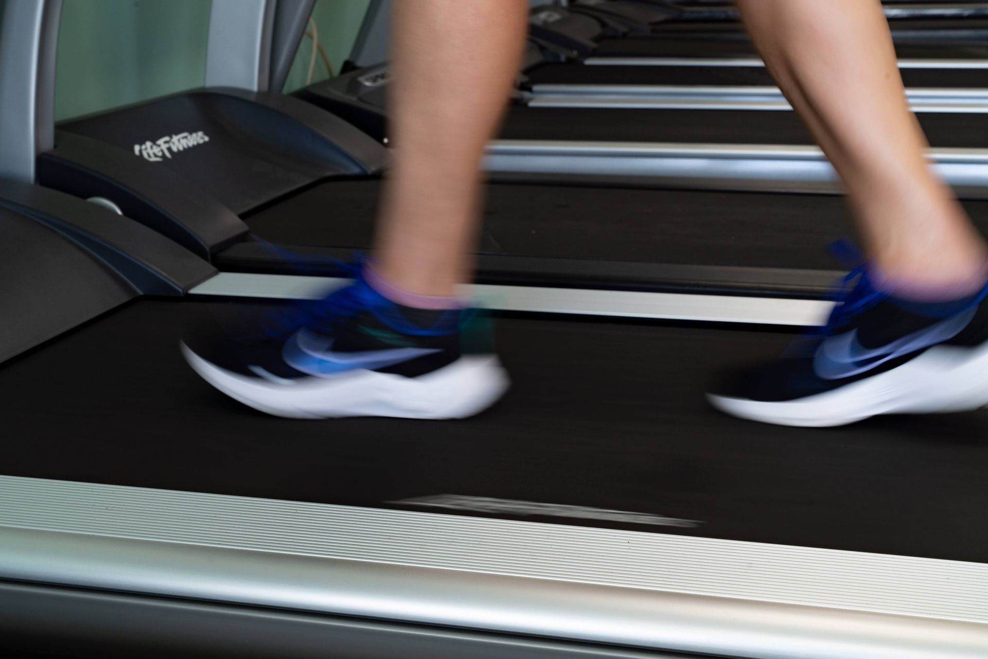 Legs in athletic shoes moving on a treadmill in a gym.