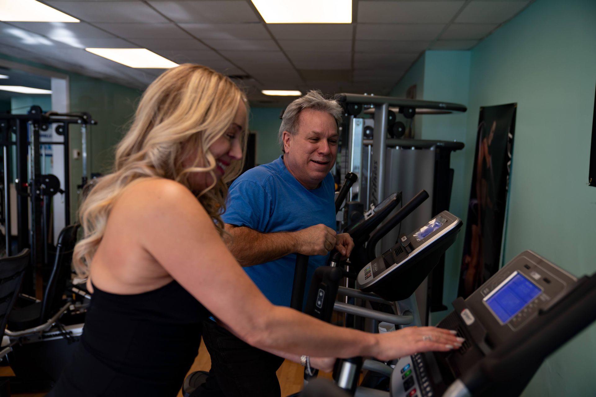 Two people in a gym using elliptical machines.
