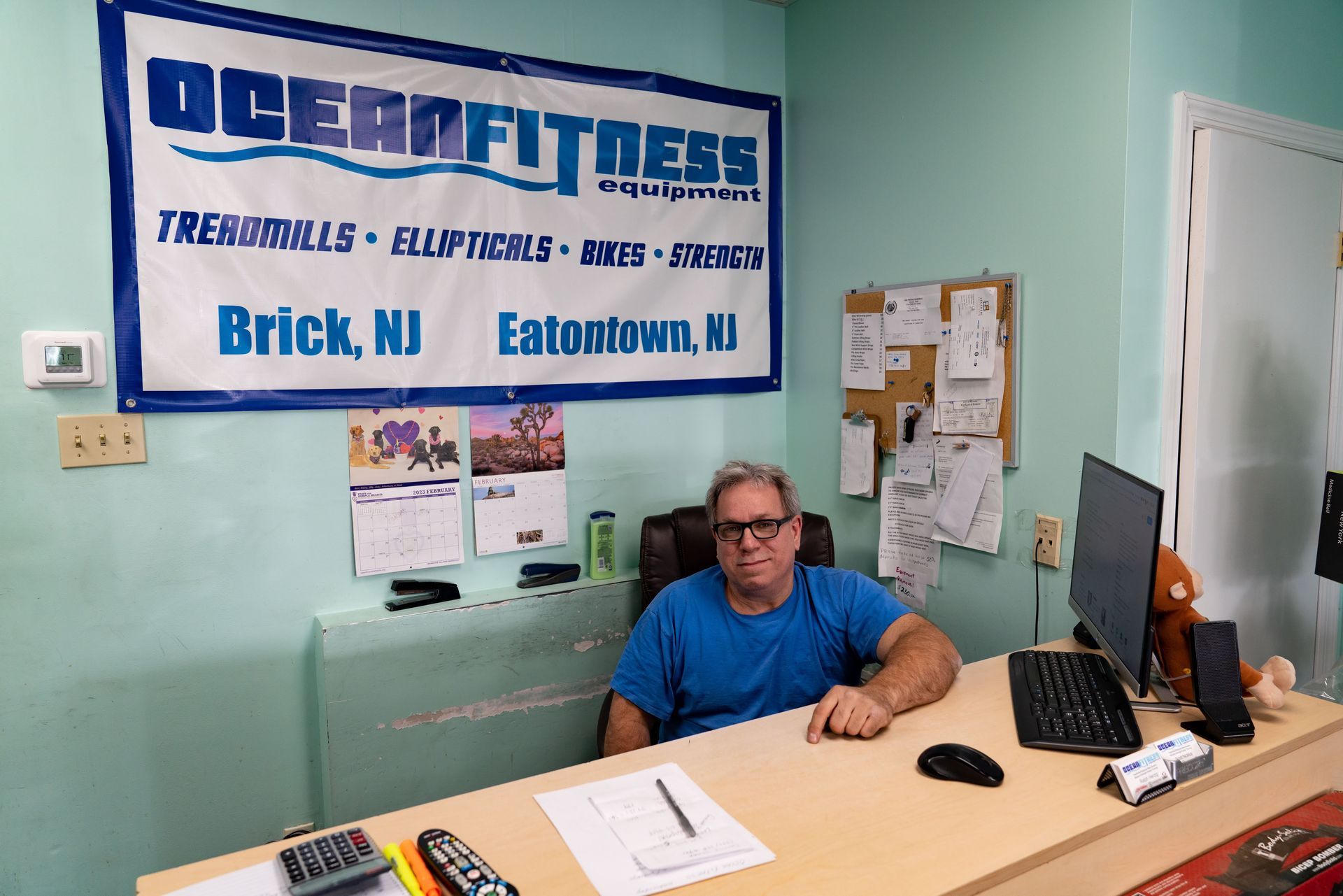 A person sits at a desk in an office with an Ocean Fitness sign on the wall behind them.