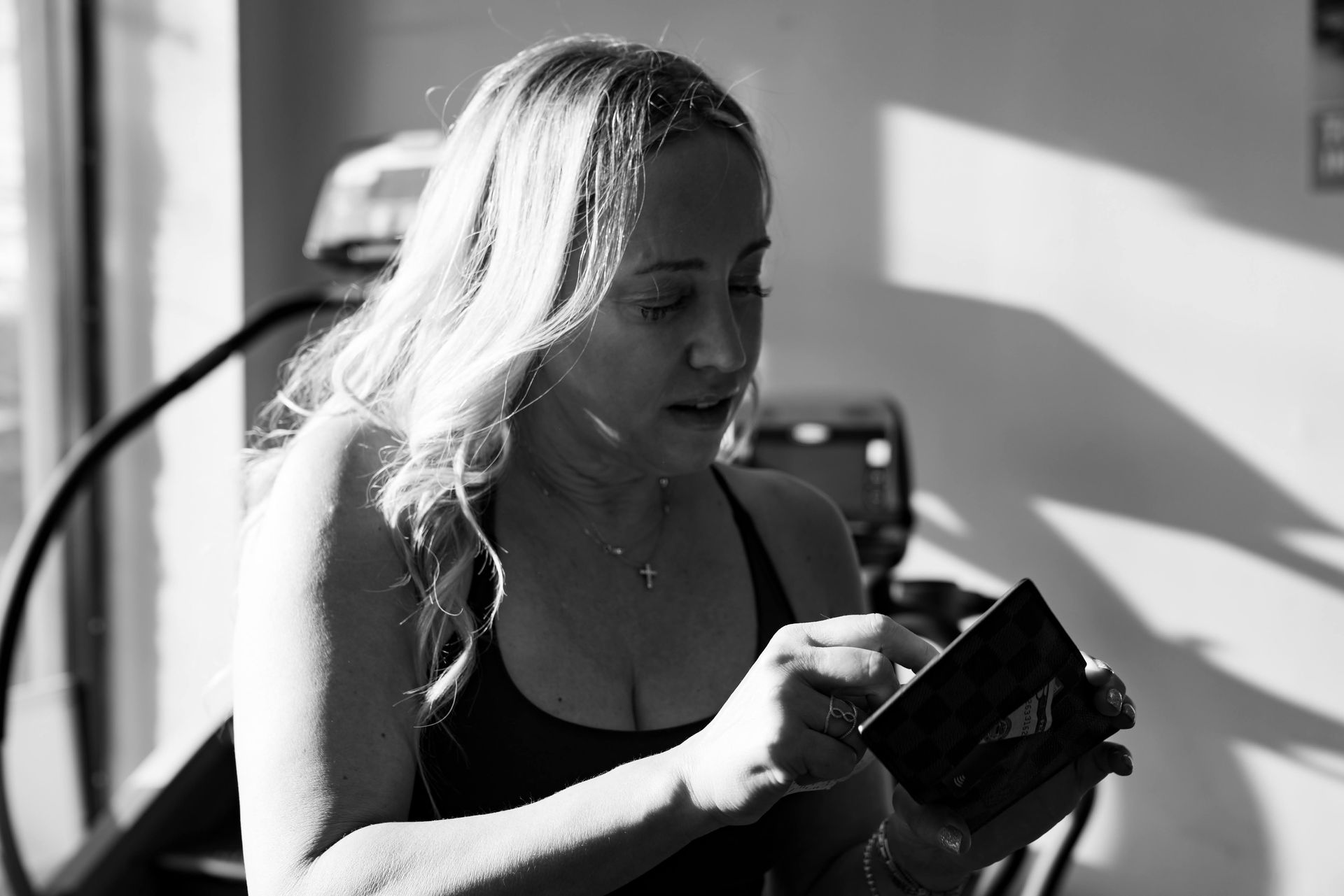 A person in workout gear holds a small, rectangular object while looking down at it, standing in a brightly lit gym.