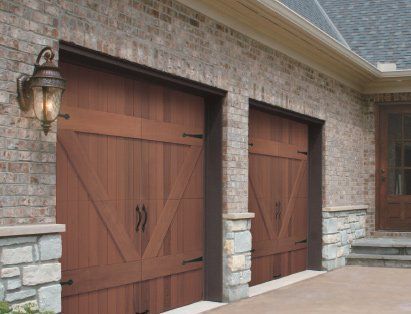 Two wooden garage doors are on the side of a brick building.