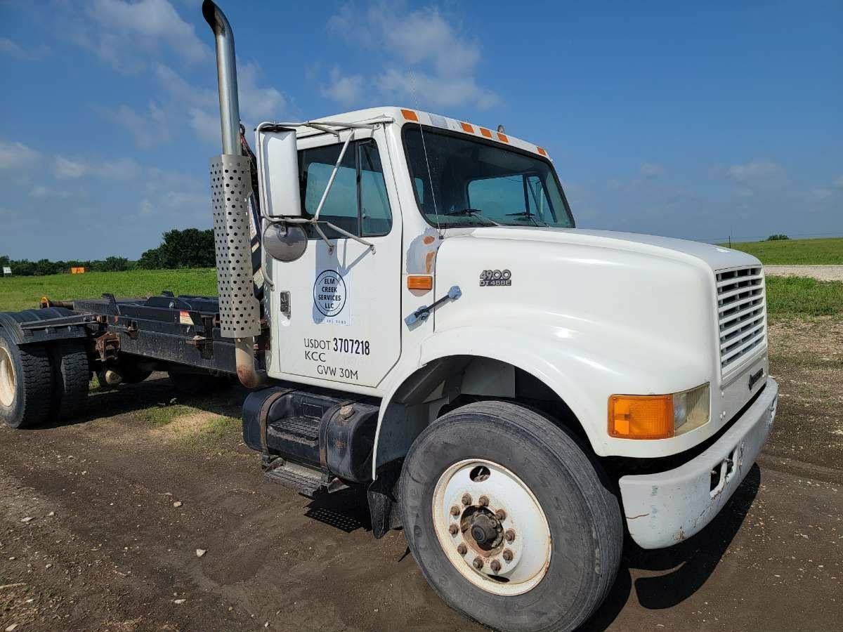 A white semi-truck cab parked on a dirt lot under a blue sky.