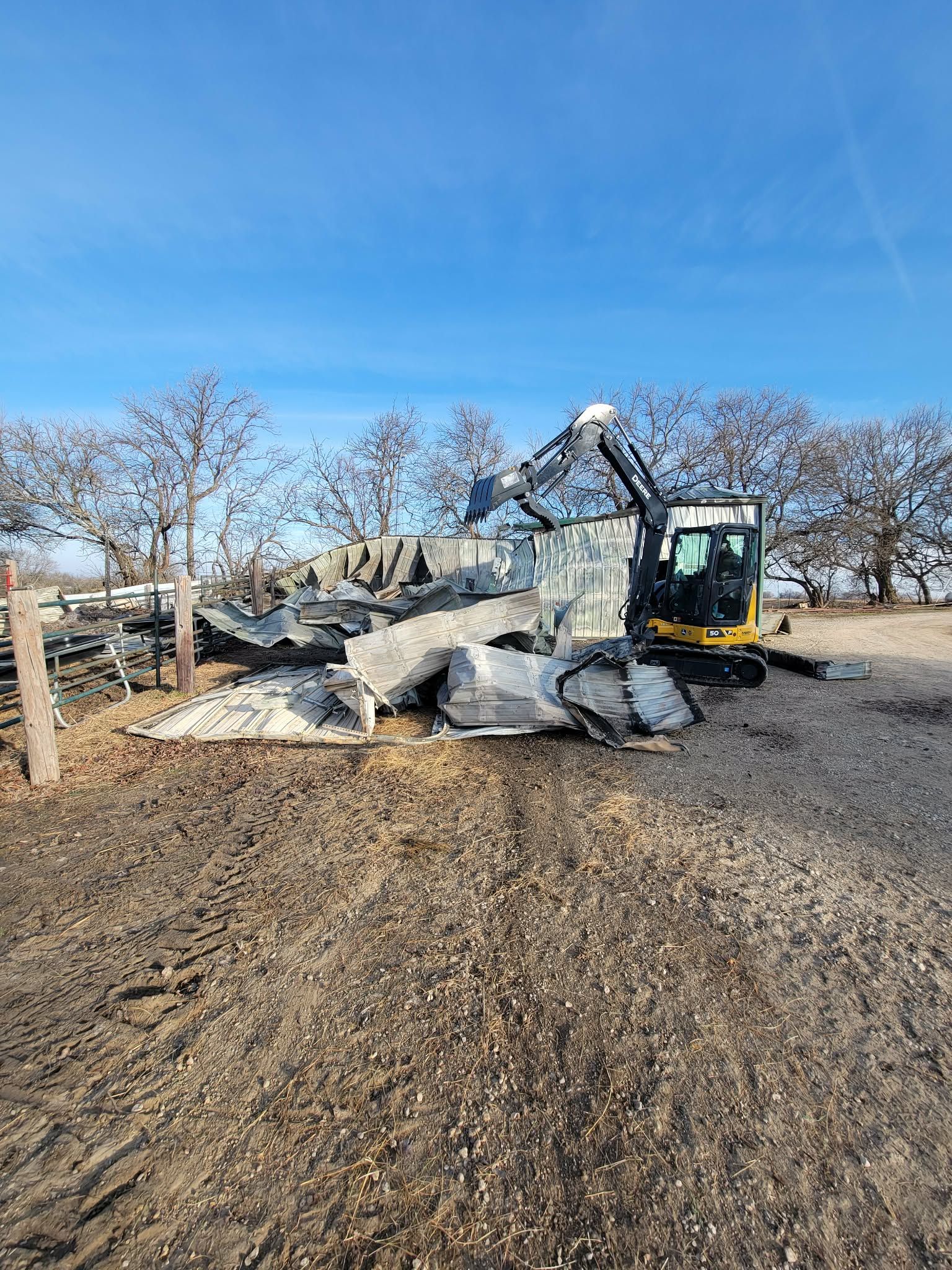 A yellow construction excavator demolishes debris on a cleared, barren lot under a bright blue sky.