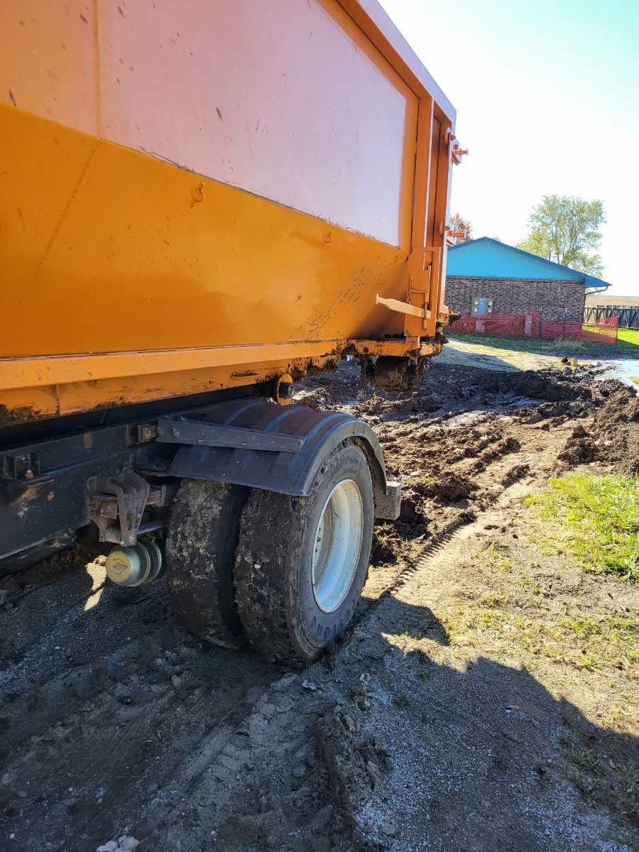 An orange dump truck parked on a muddy ground next to a stone building.
