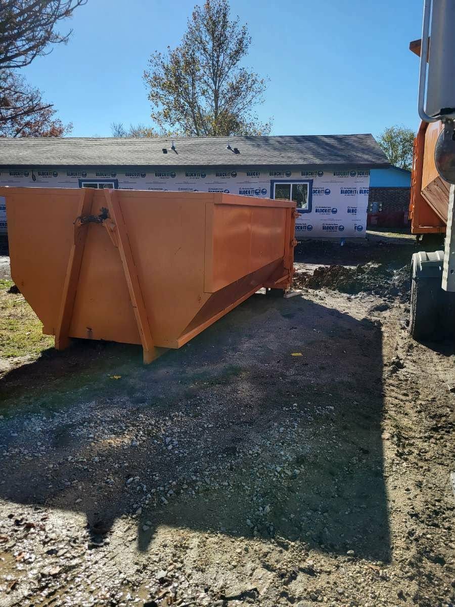 An orange dumpster sits on gravel in front of a building under construction on a sunny day.