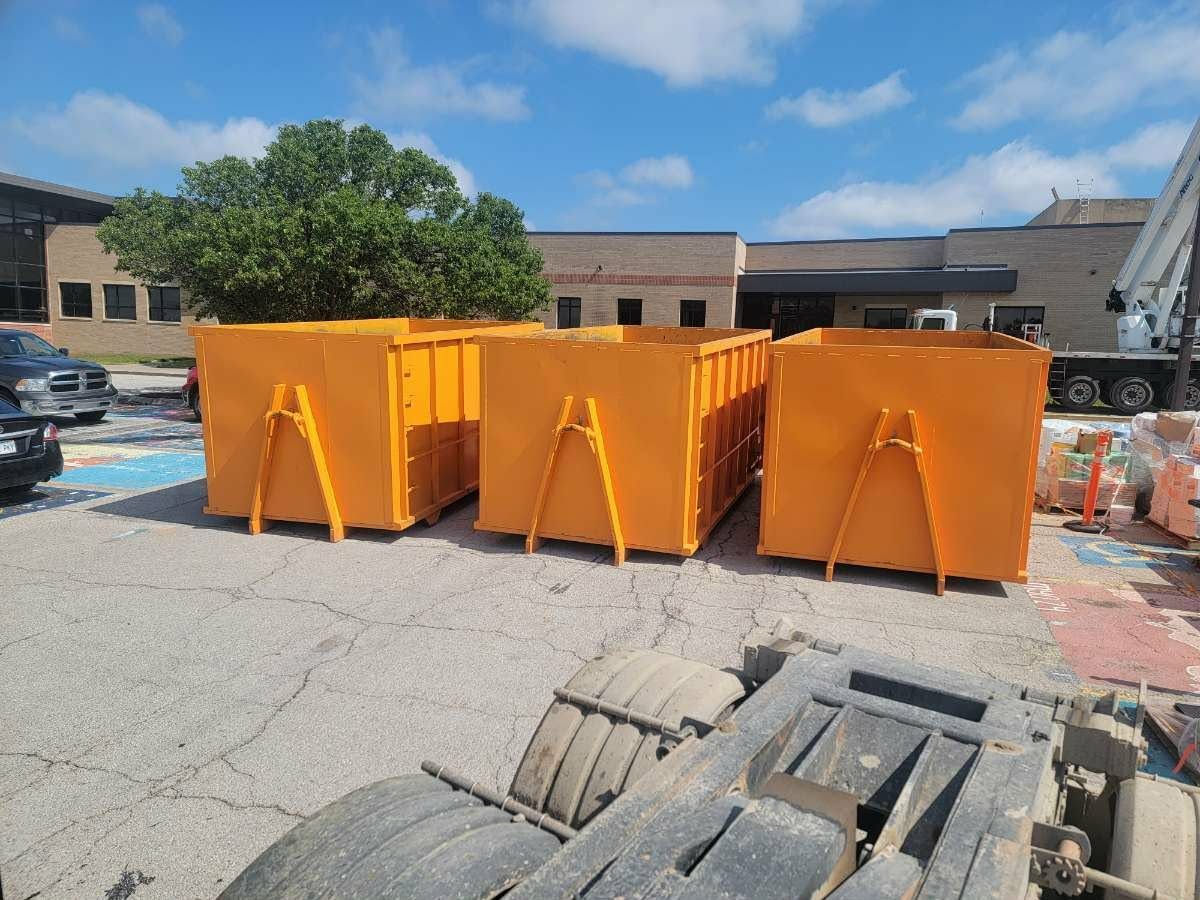 Three large, bright orange industrial dumpsters sit in a paved parking lot on a sunny day.