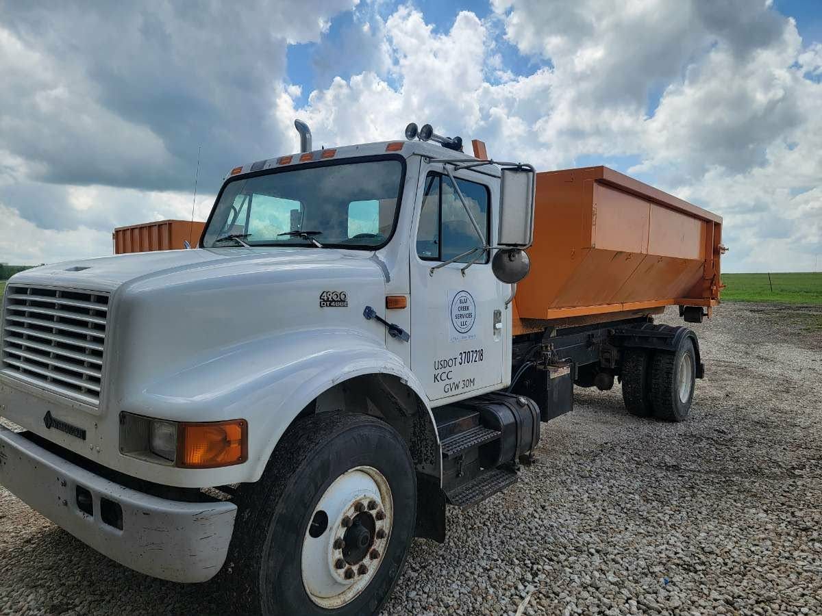 White dump truck with an orange cargo bed parked on a gravel lot under a cloudy sky.
