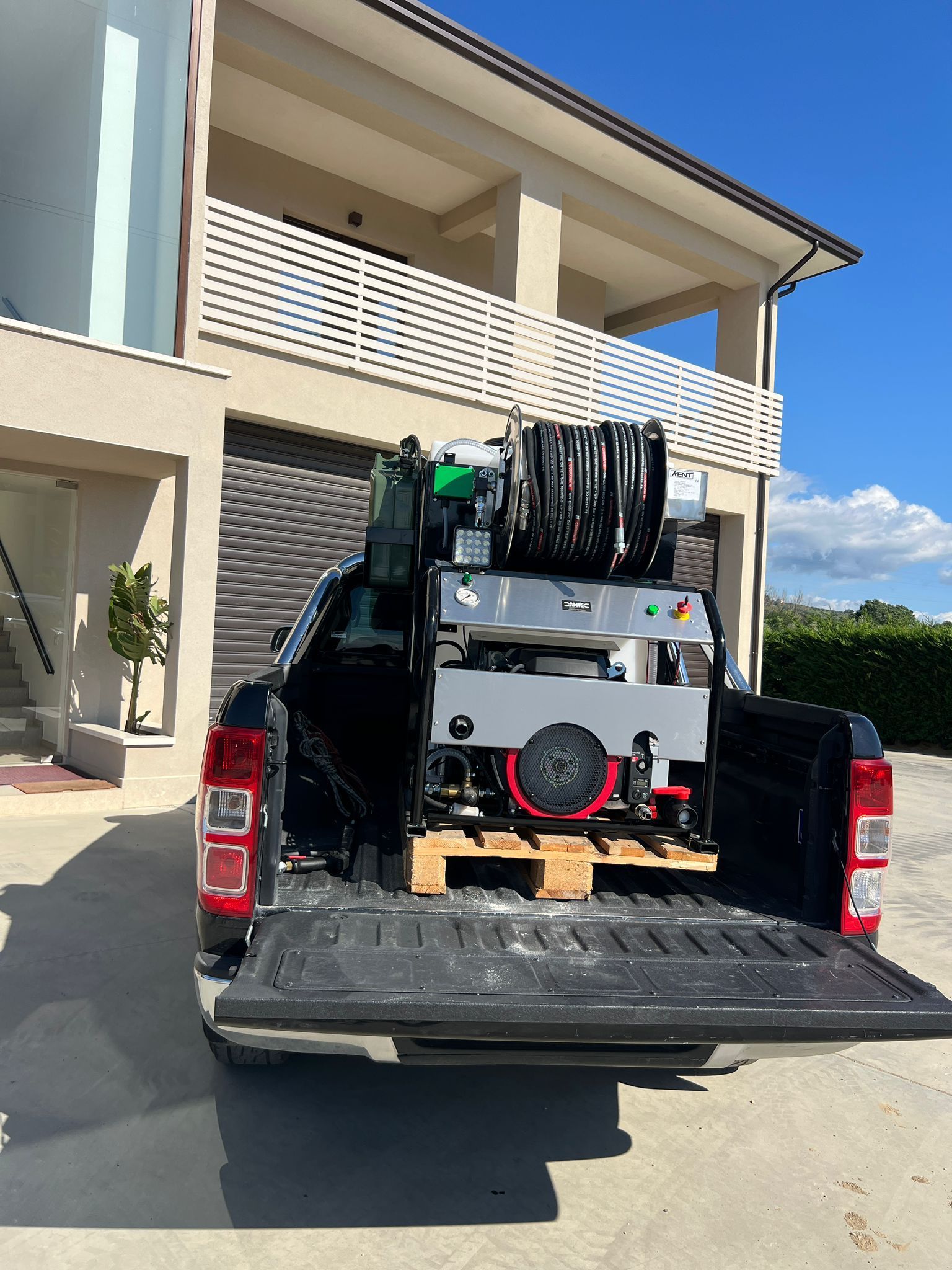 Un pick-up carico di attrezzature e tubi flessibili è parcheggiato fuori da una casa moderna.