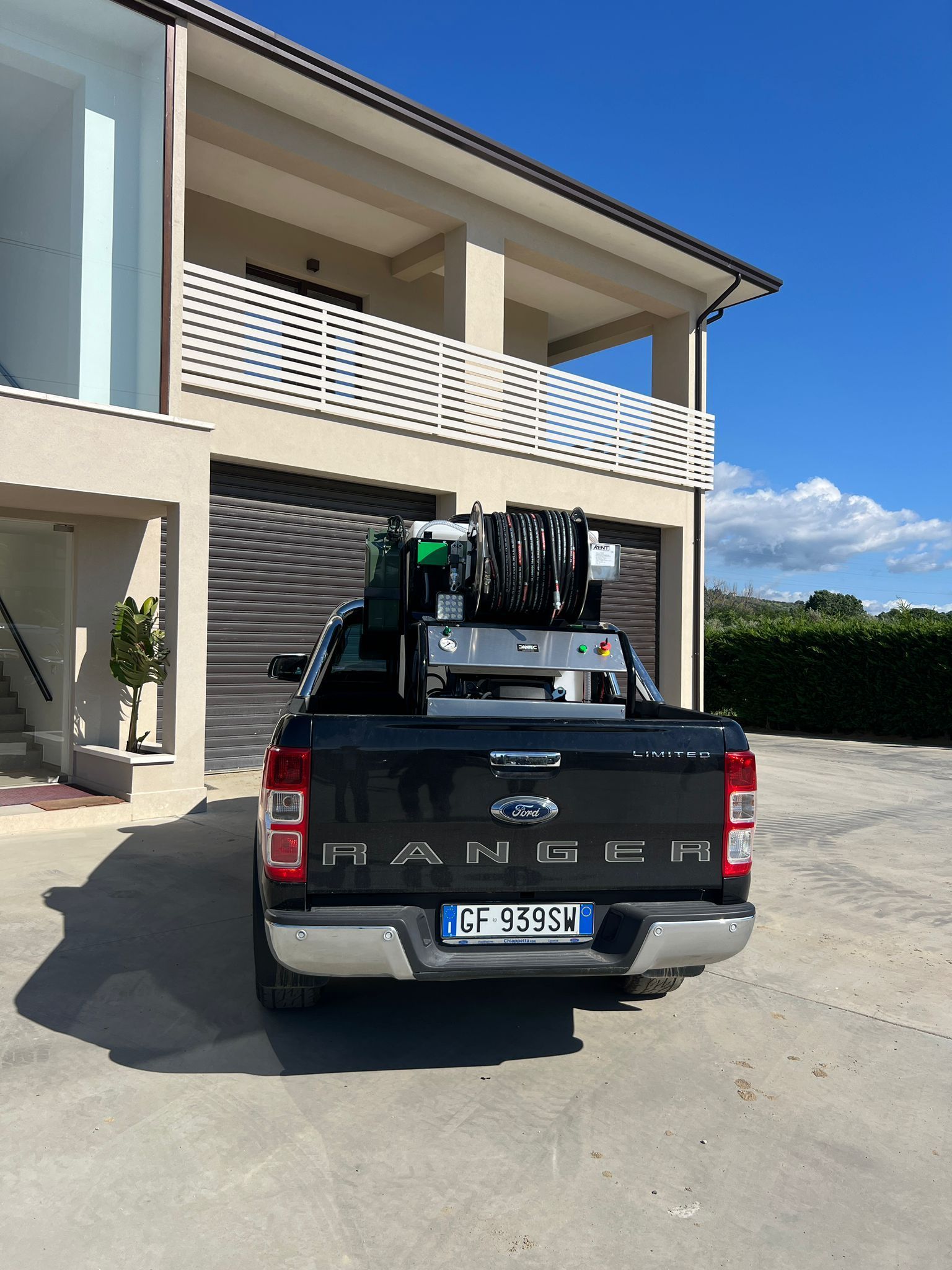 Un pick-up Ford nero, carico di attrezzature, parcheggiato sotto il sole davanti a un edificio moderno.
