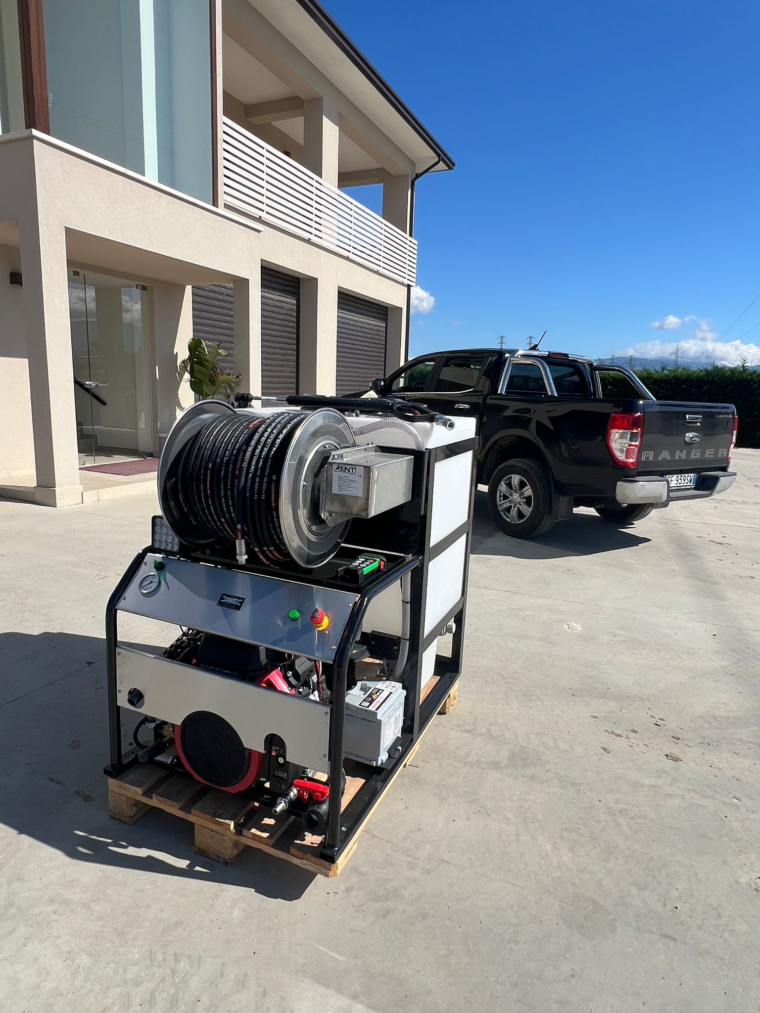 Carrello di servizio nero con tubi e attrezzature accanto a un pick-up nero in un vialetto vicino a un edificio