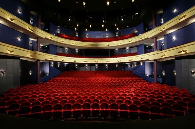 Leeg theaterinterieur met rode stoelen, balkons en uitzicht op het podium.