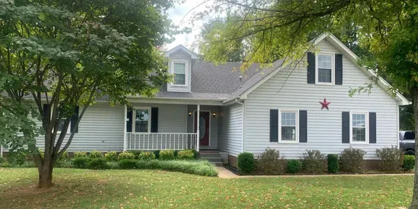 White suburban house with gray shutters, front porch, and a large tree in the yard