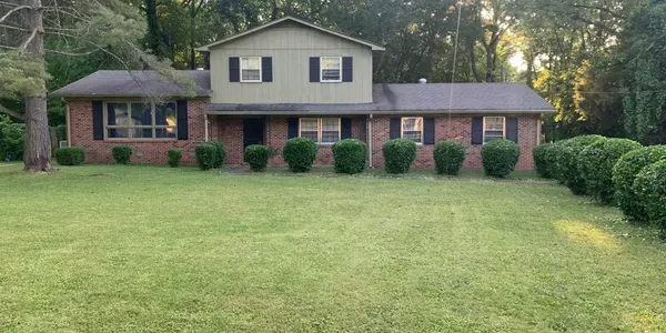 Suburban brick house with a large green lawn and trees in the background