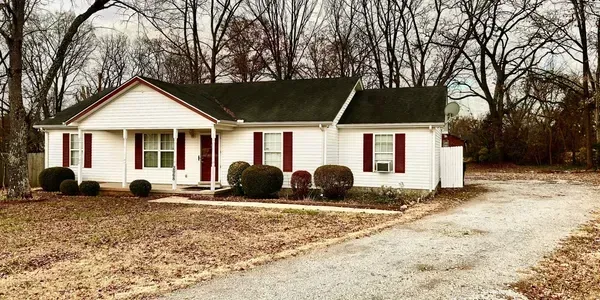 White single-story house with red shutters, front porch, and gravel driveway in a leafless yard