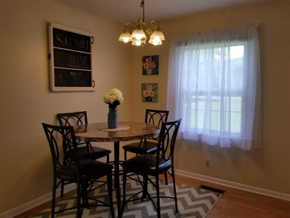 Dining nook with round table, four chairs, chandelier, wall art, and a large window with sheer curtains.