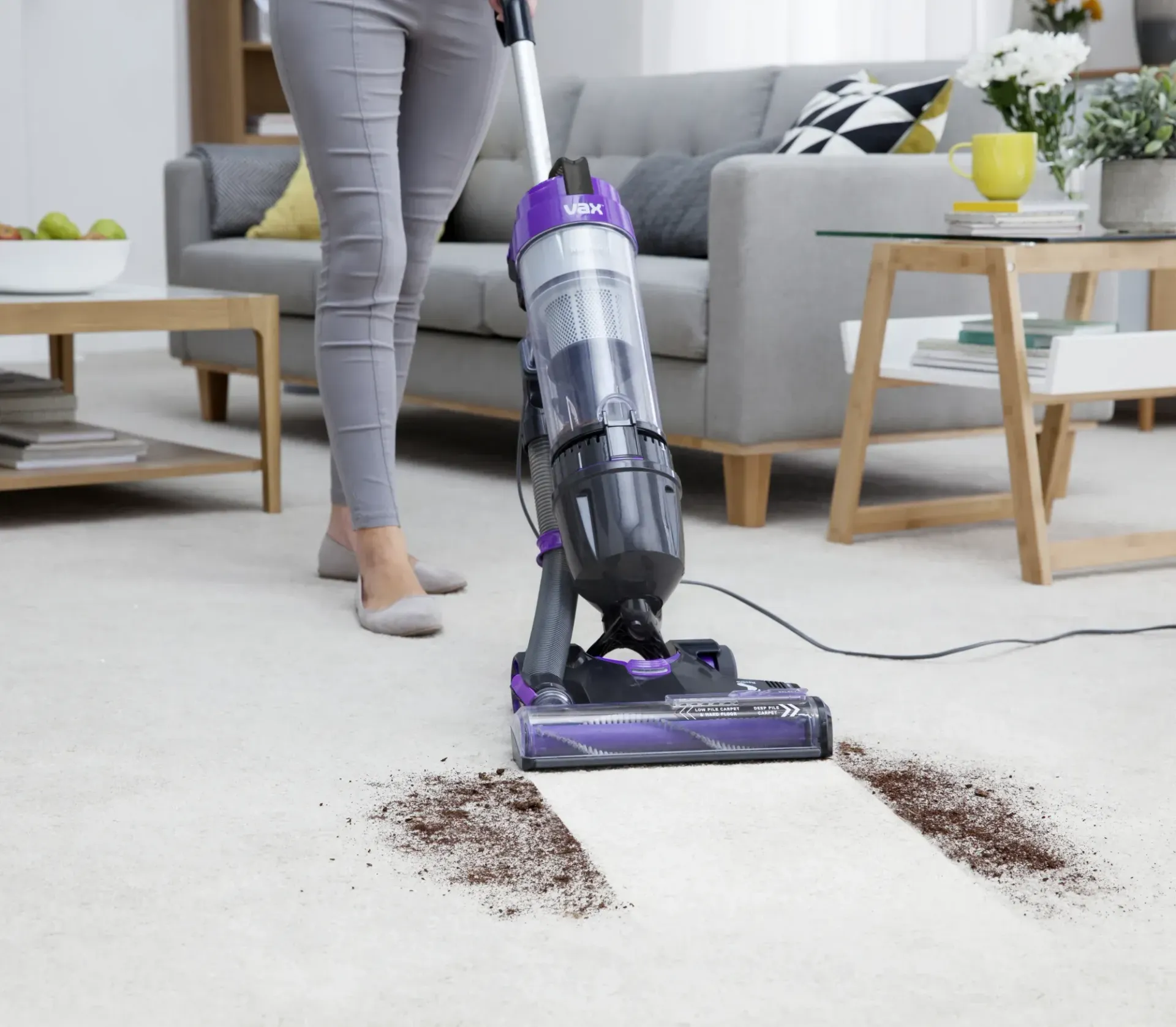 A woman is using a purple vacuum cleaner in a living room