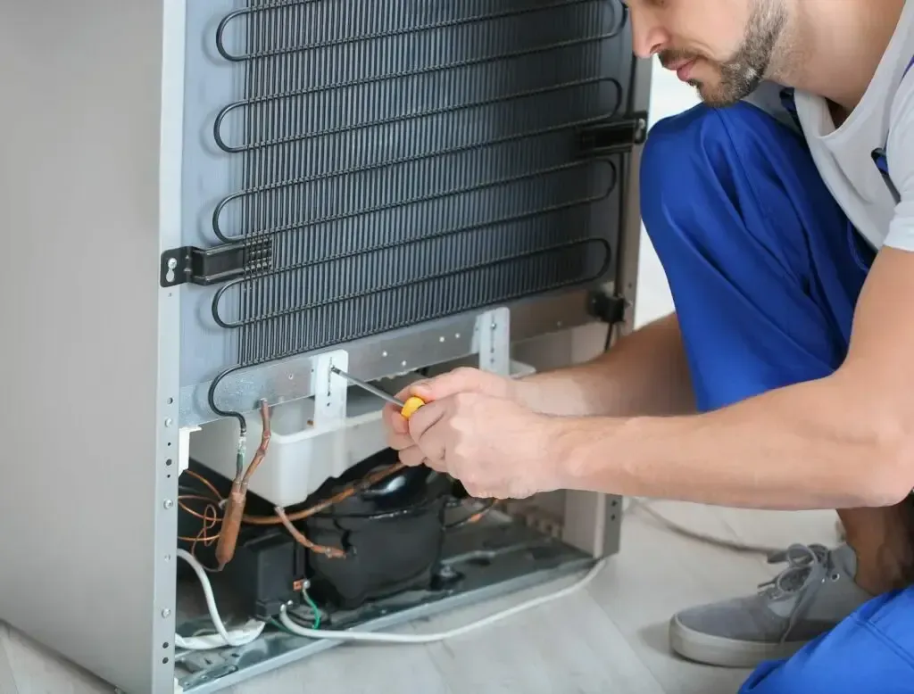 A man is fixing a refrigerator with a screwdriver.