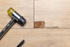 Hammer and chisel beside a small damaged spot in a wooden floorboard.