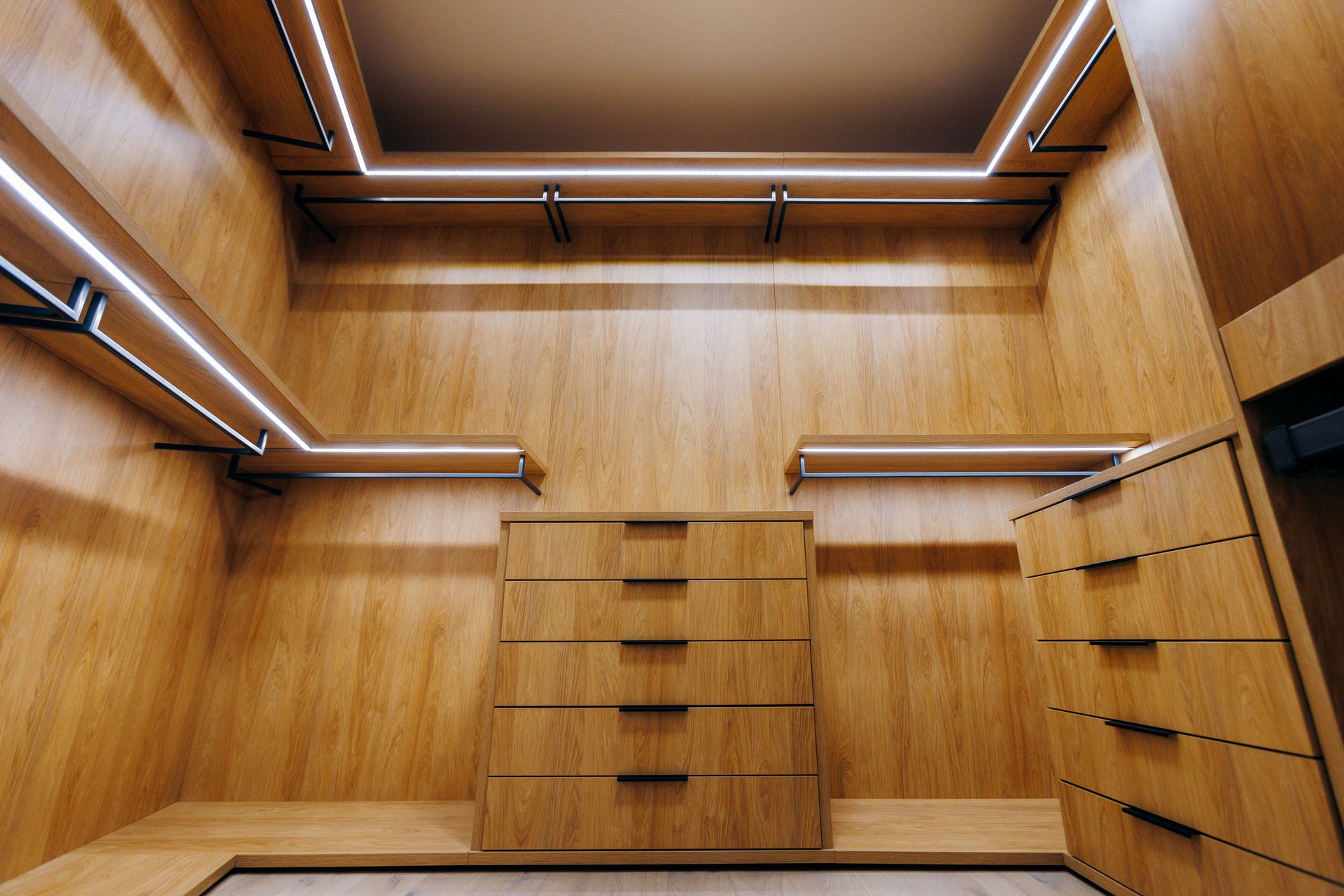 Empty wooden walk-in closet with shelves, drawers, and built-in LED strip lighting