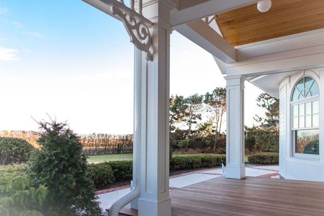 Porch with white columns and wood ceiling overlooking a landscaped yard at sunset