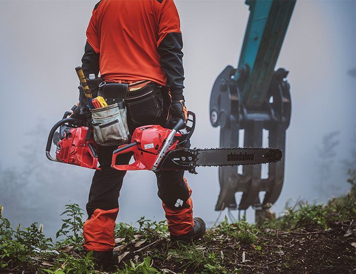 A Man is Holding a Chainsaw in His Hand While Standing on a Hill — Diamond Service Centre In Lismore, NSW