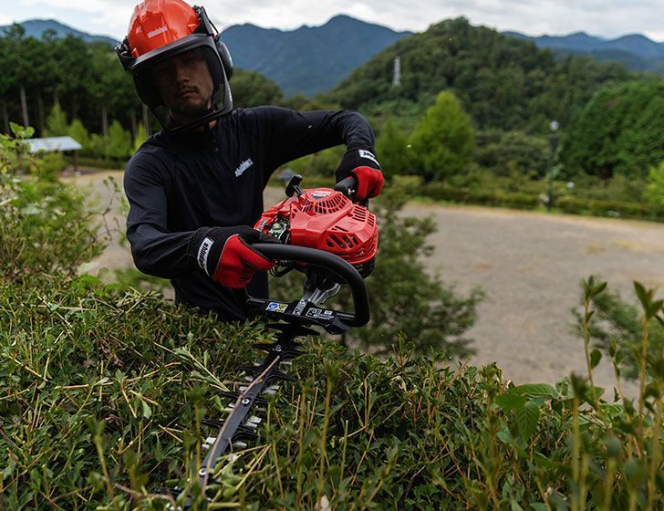 A Man Wearing a Helmet is Cutting a Bush With a Hedge Trimmer — Diamond Service Centre In Lismore, NSW