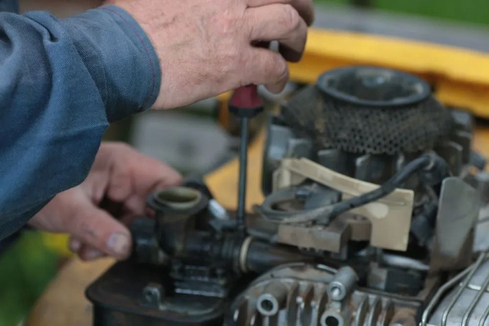 A Man is Working on a Lawn Mower Engine With a Screwdriver — Diamond Service Centre In Lismore, NSW