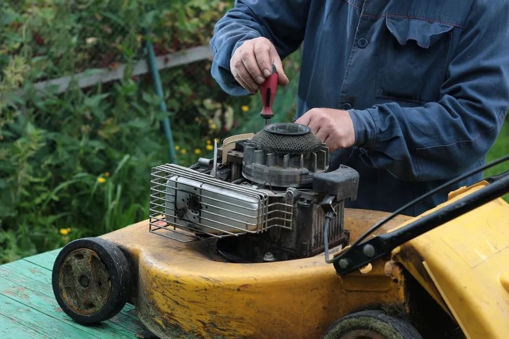 A Man is Fixing a Lawn Mower With a Screwdriver — Diamond Service Centre In Lismore, NSW