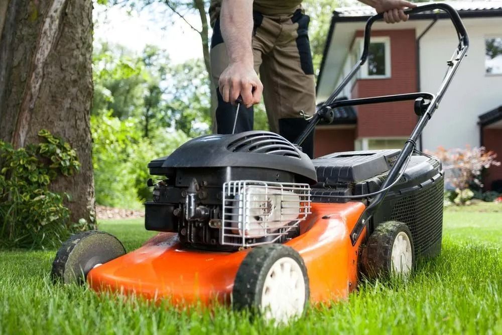A Man is Pushing an Orange Lawn Mower on a Lush Green Lawn — Diamond Service Centre In Lismore, NSW