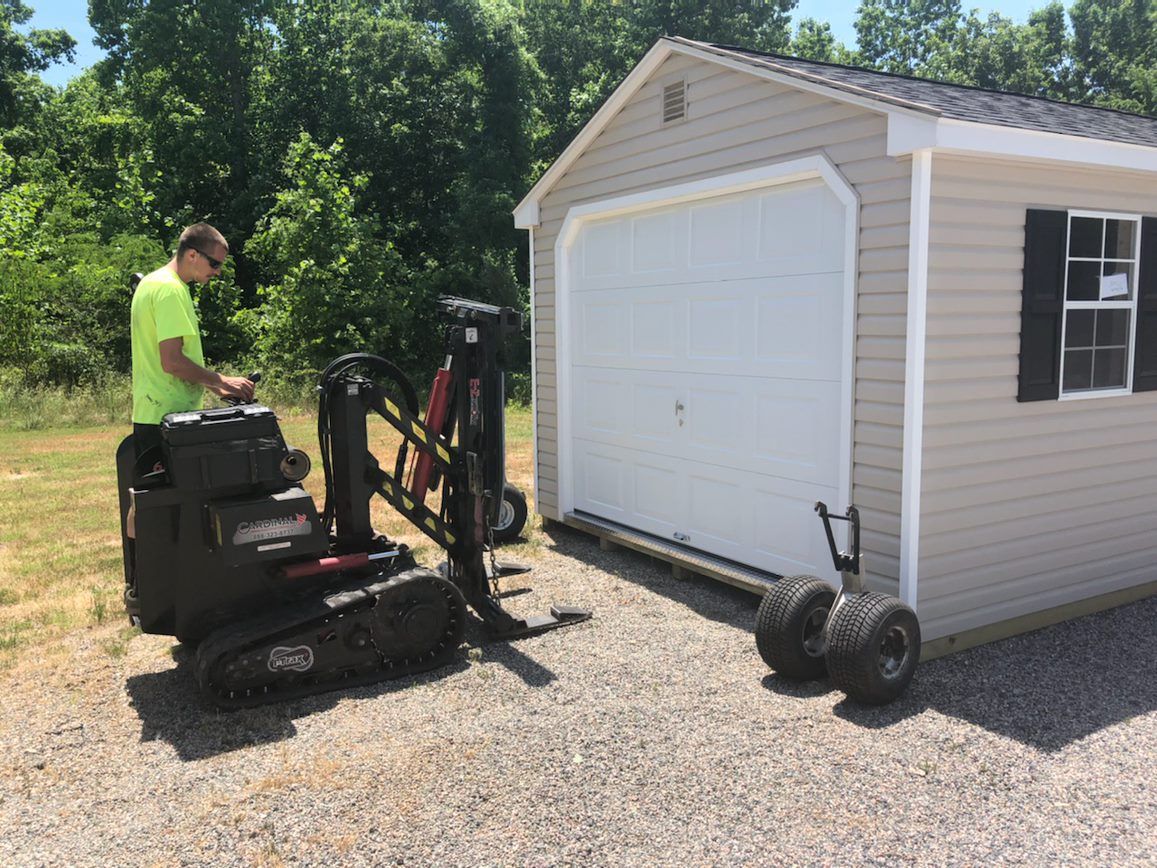 White modular building with black shutters on gravel, being moved by a forklift in a yard