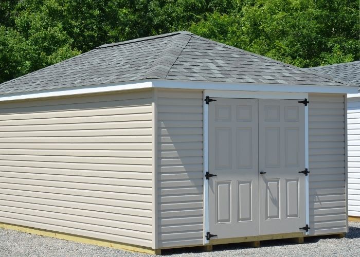 Almond vinyl garden shed with gray shingled roof and double doors on a grassy property.