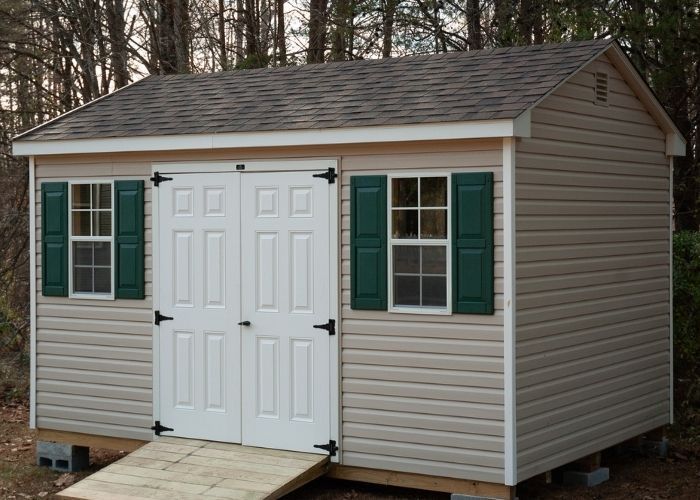 Antique ivory storage shed with white double doors, green shutters, and a ramp in front