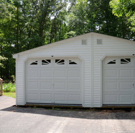 White two-car garage with arched doors in a wooded driveway