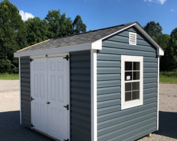 Small gray-and-white backyard shed with double doors and a window under a blue sky