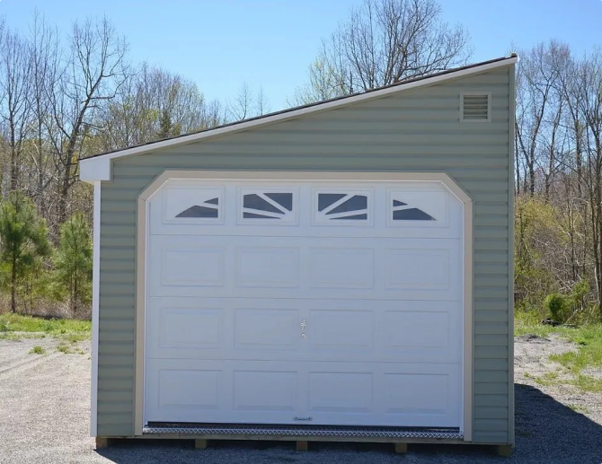 Small beige shed with a white garage door in a wooded outdoor setting.