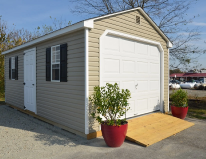 Small beige storage shed with white garage-style door and red planters outside