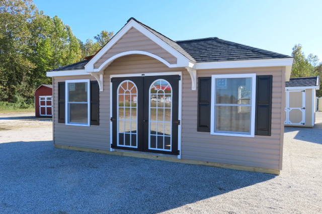 Small tan house with black double doors, white trim, and a gabled front porch on gravel