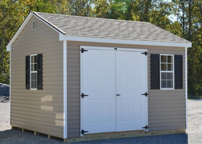 Khaki shed with white double doors and black shutters on a gravel lot