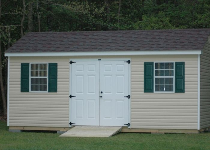 Linen shed with white double doors and green shutters on a grassy lawn.