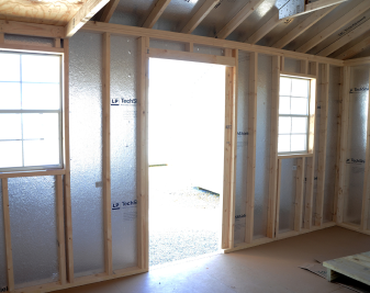 Unfinished interior of a house under construction with exposed framing and bright doorway and windows.