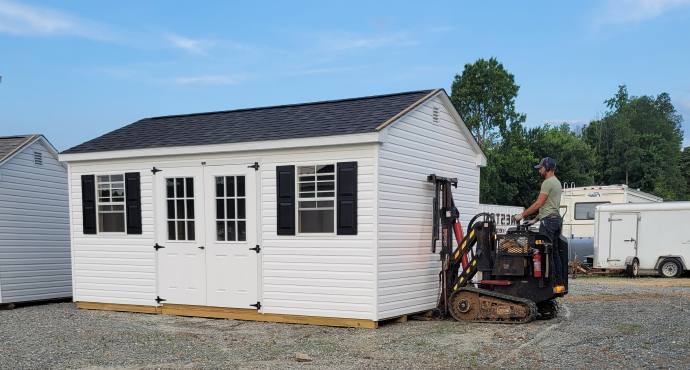 Worker operating a compact loader beside a white modular building with black shutters and a dark roof