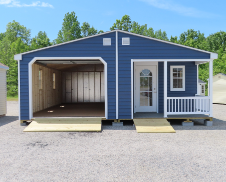 Blue garage with open bay, white trim, and small porch, shown on a gravel lot under a clear sky