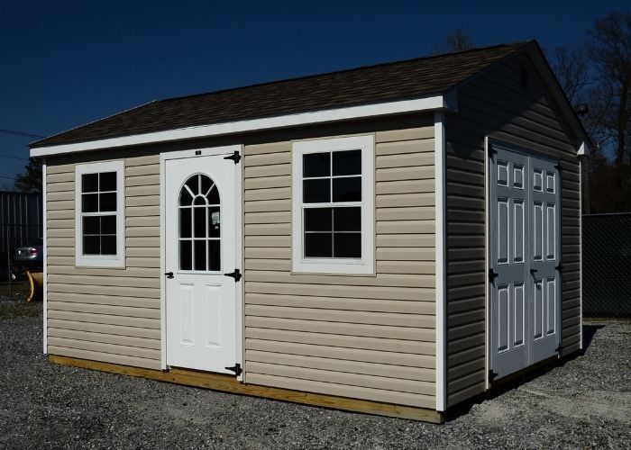 Sandstone storage shed with white doors and windows on a gravel lot under a clear blue sky