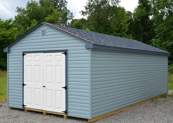 Slate blue storage shed with white double doors on a gravel lot
