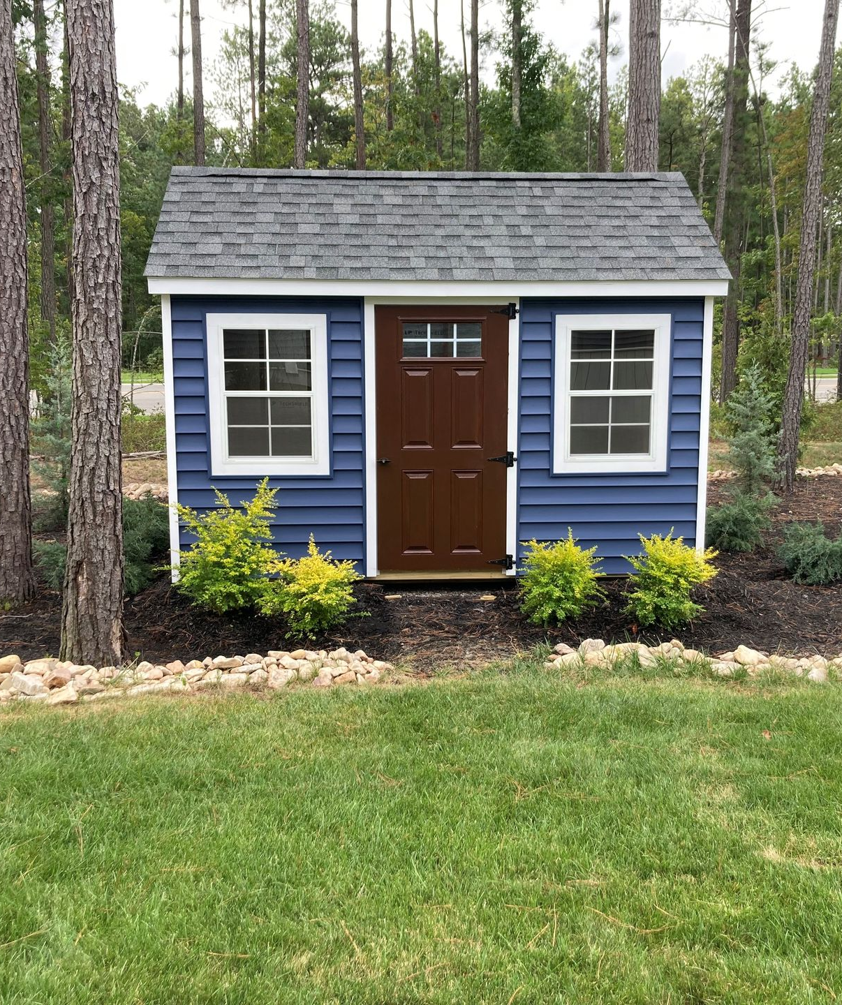 Small tan house with black double doors, white trim, and a gabled front porch on gravel