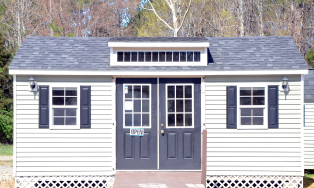 Small white cottage-style house with black shutters, dark double doors, and a peaked gray roof.